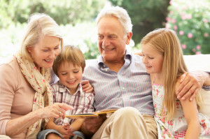 Portrait Of Grandparents Reading To Grandchildren On Sofa